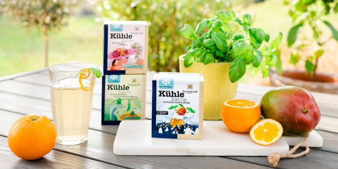 Auf dem Foto sind die Kühle Kanne Teepackungen zu sehen. Daneben liegt frisches Obst. | © SONNENTOR