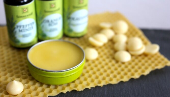 Jarolim Wander Balsam | © SONNENTOR Auf dem Foto ist eine kleine dose mit Wander Balsam zu sehen. Gemeinsam mit den ätherischen Ölen steht sie auf einer Honigwabe. | © SONNENTOR
